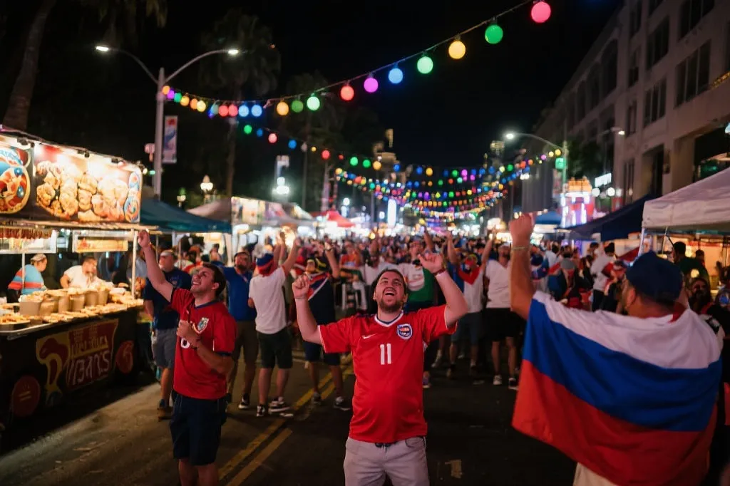 洛杉矶街头夜间观赛派对，彩灯与摊位，人群穿着各国球衣欢呼，纪录片风格